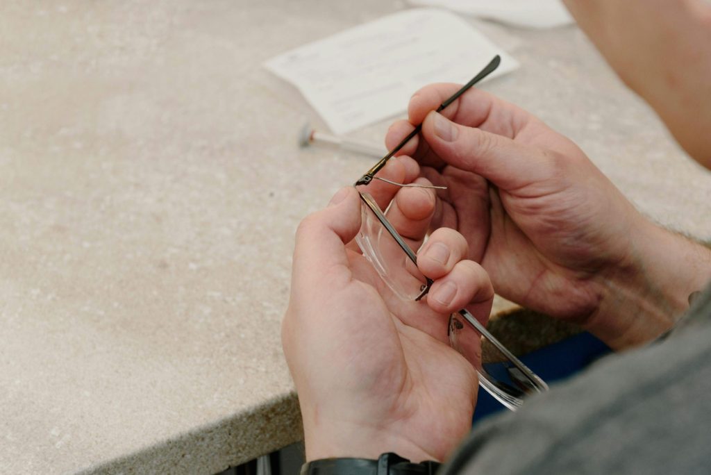 Vue de dessus d'un maître opticien anonyme assis à une table, fixant une branche de lunettes avec une vis lors de la réparation de ses lunettes dans un atelier professionnel.