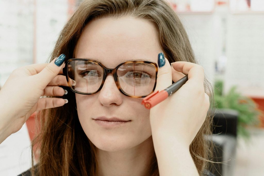 Anonymous female oculist putting modern eyewear on young woman during consultation in clinic
